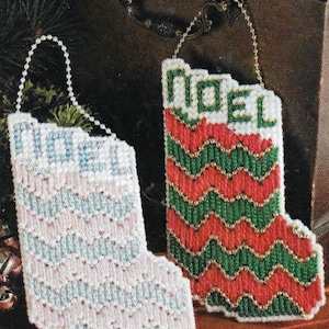 Pode incluir: Duas meias de Natal brancas com um padrão em ziguezague e a palavra "Noel" bordada nelas. A meia à esquerda tem um padrão azul e rosa, enquanto a meia à direita tem um padrão vermelho e verde.