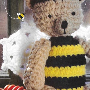 Puede incluir: Un oso de peluche de crochet vestido de abeja. El oso es marrón con un chaleco a rayas negro y amarillo. El oso tiene una nariz negra y ojos negros. El oso está sentado sobre una superficie de madera.