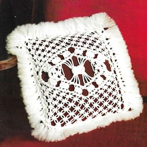 Op de afbeelding: Wit gebreid kussen met een franje rand. Het kussen heeft een vierkante vorm en een delicaat, ingewikkeld ontwerp in het midden.