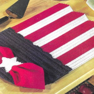 May include: A red, white, and blue crocheted table runner with a white star and red bow. The runner is made with a textured yarn and has a scalloped edge.
