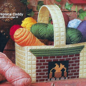 May include: A white plastic yarn caddy with a fireplace design. The caddy has a handle and is filled with colorful yarn balls. The text "Fireplace Caddy" and "Instructions on page 28" is printed on the image.