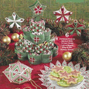 Pode incluir: Seis projetos de tela de plástico com tema natalino, incluindo um prato de doces em camadas com formato de árvore de Natal, um enfeite em forma de estrela e uma caixa geométrica. Todos os projetos são costurados com fio vermelho, verde e branco.