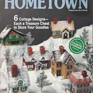 Peut inclure: Un livre de patrons en plastique canevas intitulé "Hometown" présentant six modèles de cottages. La couverture montre des maisons miniatures avec des cheminées rouges et des toits enneigés. Le texte indique "Each a Treasure Chest to Store Your Goodies."