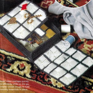 May include: A white and black plastic sewing kit shaped like a cell phone. The kit has a hinged lid with a gold and white design. The kit is open and shows the compartments inside. The kit is on a red and gold patterned rug.