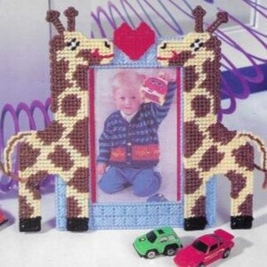 May include: A wooden picture frame with two giraffes on either side of a red heart. The frame is decorated with brown and yellow spots. A photo of a child is in the frame.