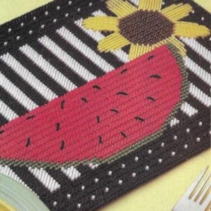 Pode incluir: Um tapete de mesa listrado preto e branco com uma melancia vermelha e um girassol amarelo. O tapete de mesa tem bolinhas brancas ao redor da borda.