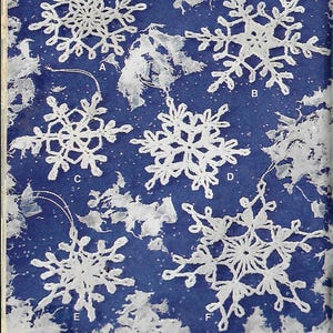May include: Six white crocheted snowflakes on a blue background. The snowflakes are all different designs and are hanging from strings. The snowflakes are labelled with letters A through F.