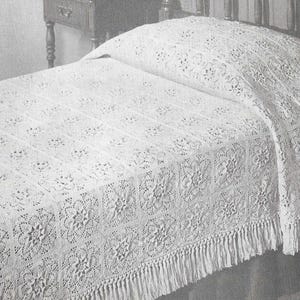 Puede incluir: Una colcha de cama blanca de ganchillo con un borde de flecos. La colcha tiene un delicado patrón floral y está hecha de hilo fino.