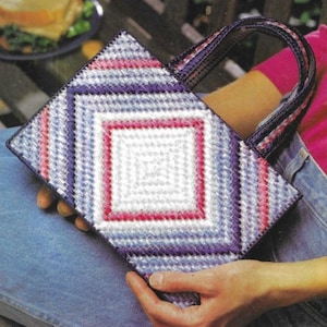 May include: A white canvas tote bag with a diamond pattern in shades of pink, blue, and purple. The bag has two handles and is held by a person.