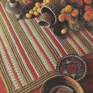 Puede incluir: Una alfombra de crochet con rayas marrones, blancas y rojas. La alfombra está sobre una superficie roja y hay varias cestas tejidas y limones sobre la alfombra.