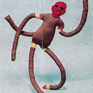 May include: A brown fabric monkey toy with red and yellow striped arms and legs. The monkey has a red face with black eyes and a black mouth.