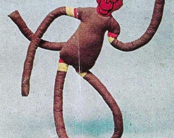 May include: A brown fabric monkey toy with red and yellow striped arms and legs. The monkey has a red face with black eyes and a black mouth.