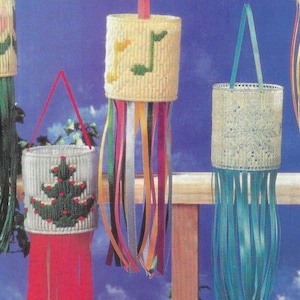 May include: Four colourful, handmade wind chimes with different designs. Each chime is made of a white plastic cylinder with a crocheted design and has multiple ribbons hanging from the bottom. The designs include a musical note, a flower, a Christmas tree, and a snowflake.
