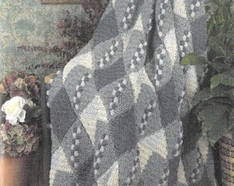 May include: A crocheted throw blanket in shades of gray and white with a diamond pattern. The blanket is draped over a chair.