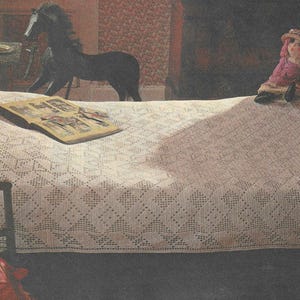 May include: A white crocheted bedspread with a diamond pattern. A book and a doll are on the bedspread.