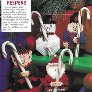 May include: Five different Christmas characters made of plastic canvas, each holding a candy cane. The characters include a snowman, a soldier, an elf, Santa Claus, and a gingerbread man.