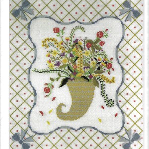 Puede incluir: Un patrón de punto de cruz que presenta una cornucopia desbordante de flores y bayas coloridas. La cornucopia está rodeada por un borde azul y blanco y un fondo a cuadros verde y blanco.