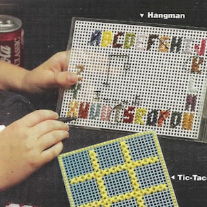 May include: A close-up of two craft projects. The first is a white plastic canvas with a grid pattern and colorful embroidery floss forming the letters of the alphabet. The second is a plastic canvas with a grid pattern and yellow and blue embroidery floss forming a tic-tac-toe board. The text "Hangman" and "Tic-Tac-Toe" are printed on the image.