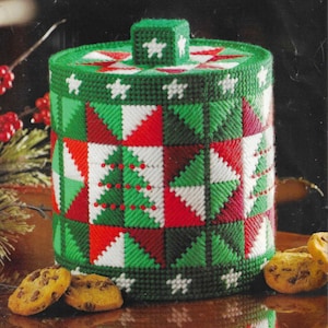 May include: A green, red, and white Christmas-themed cookie jar with a square lid. The jar features a patchwork design with Christmas trees and star accents. Chocolate chip cookies are in front of the jar.