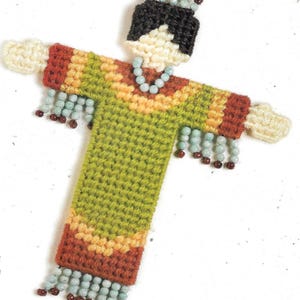 May include: A green, yellow, and brown yarn doll with a black yarn head and a crown of beads. The doll is wearing a necklace of blue beads and has long, beaded fringe on the sleeves and bottom of the dress.