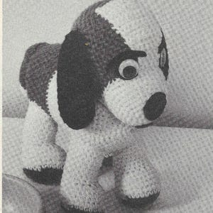 May include: A black and white crocheted dog toy with large plastic eyes. The dog is standing on a textured surface.