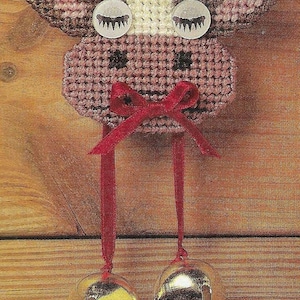 Puede incluir: Adorno hecho a mano con forma de vaca con cuerpo en forma de campana y un lazo rojo decorativo. El adorno está hecho de un material tejido con una campana de metal y está diseñado para colgar. La vaca tiene ojos de botón.