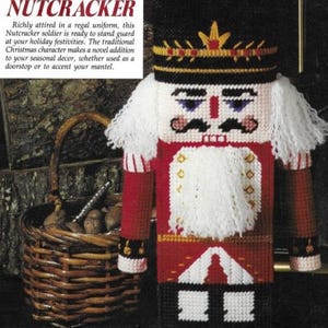 May include: A white, red, and black Christmas nutcracker doll with a white beard and mustache. The nutcracker is wearing a black hat with a gold crown and a red and white uniform. The nutcracker is standing in front of a wicker basket filled with nuts.
