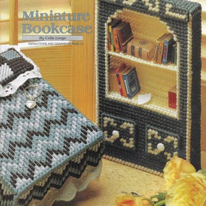 Peut inclure: Une petite bibliothèque miniature avec deux étagères et un tiroir. La bibliothèque est faite de toile plastique et est décorée de perles blanches. La bibliothèque est remplie de livres miniatures. Le texte "Miniature Bookcase" est imprimé sur la page.