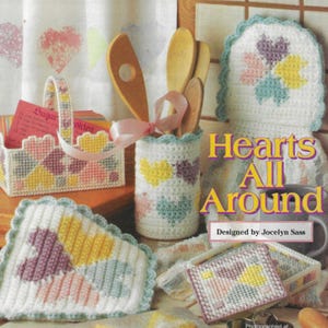 May include: A set of colorful crocheted items featuring a heart pattern. The set includes a utensil holder, a basket, a hot pad, and a small box. The title "Hearts All Around" is displayed on the image.