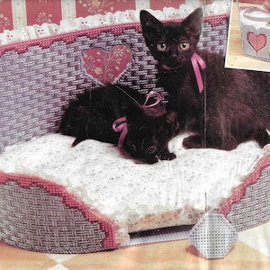May include: A white and pink woven pet bed with a white cushion and two black kittens. The bed has a heart-shaped design and a lace trim.