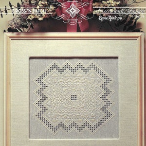 Puede incluir: Un diseño de punto de aguja blanco enmarcado con un patrón circular de puntadas blancas y grises. El diseño se titula "Needlework Fantasy" de "Emme Bishop" No. 76.