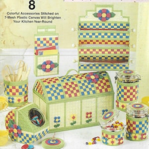 May include: A set of eight colorful plastic canvas kitchen storage containers with a checkered pattern and floral accents. The containers include a utensil holder, a bread box, a canister, a spice rack, and a small container with a lid. The containers are all decorated with yellow, red, blue, and green flowers.
