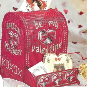 May include: Red plastic canvas mailbox with a drawer. The mailbox has a heart design with the words "Be My Valentine" and "XOXO" on the front. The drawer has three hearts on the front.