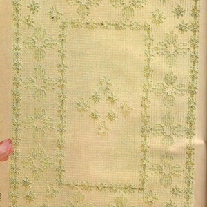 Puede incluir: Un tapiz de pared de crochet beige con un diseño floral. El tapiz tiene un borde de pequeñas flores y un diseño floral más grande en el centro.