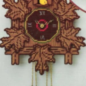 Könnte beinhalten: Eine braune Holzkuckucksuhr mit einem gelben Vogel, einem Zifferblatt mit römischen Ziffern und braunen Blättern. Die Uhr hat ein Pendel mit drei braunen eichelförmigen Gewichten.