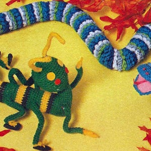 May include: A green and yellow crocheted lizard and a blue and white crocheted snake on a yellow background with red and orange leaves.