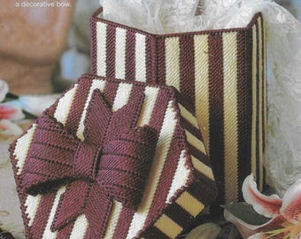 May include: A white and burgundy striped hexagonal gift box with a burgundy bow on the lid. The box is open and the lid is resting on the side. The box is made of plastic canvas.