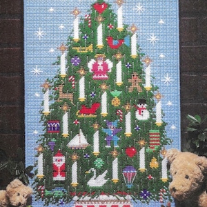 Könnte beinhalten: Ein Kreuzstich-Design eines Weihnachtsbaums mit Ornamenten, Kerzen und Sternen auf blauem Hintergrund. Zwei Teddybären befinden sich im Vordergrund.