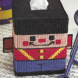 May include: A tissue box cover with a colorful design of a cartoon musician. The musician is wearing a red jacket with yellow trim, blue pants, and a black hat. The tissue box cover is made of plastic canvas and is perfect for adding a whimsical touch to any room.