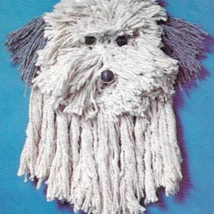 May include: A white mop head with gray ears and black eyes, shaped into a dog's face. The mop head is fluffy and has a long, shaggy mane.