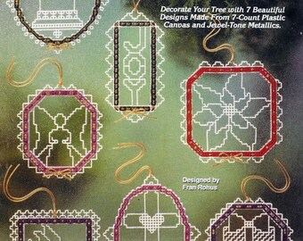 Könnte beinhalten: Sieben Kreuzstich-Ornament-Designs mit einer Glocke, dem Wort "FREUDE", einer Weihnachtsstern, einem Engel, einem Kreuz mit einem Herzen, einer Geschenkbox und einem Strumpf. Die Ornamente sind aus 7-zählgem Plastik-Canvas und Edelmetallfäden gefertigt. Der Titel "Golden Laced Ornaments" befindet sich oben im Bild. Der Text "Designed by Fran Rohus" befindet sich unten im Bild.