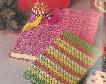 May include: Two crocheted book covers, one pink and one green with yellow, red, and white stripes. The pink cover is on top of a book.