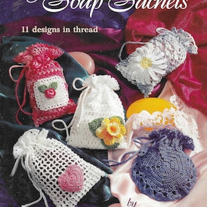 Puede incluir: Un libro de patrones de crochet titulado "Soap Sachets" con 11 diseños en hilo. La portada presenta una variedad de bolsitas de jabón de crochet en diferentes colores y diseños, incluyendo una margarita, una flor y un corazón.