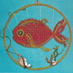 以下が含まれることがあります： 手作りの赤いかぎ針編みの魚で、黄色のアクセントが付いています。円形のフレームの中に吊り下げられています。フレームは、海藻や貝殻などの追加のかぎ針編み要素で装飾されており、ターコイズブルーの背景に配置されています。装飾品。