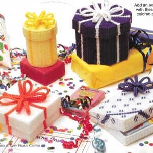 Könnte beinhalten: Eine Sammlung bunter Geschenkboxen aus Plastik-Canvas mit verschiedenen Designs, darunter eine violett-weiß gestreifte Box, eine gelb-weiß gestreifte Box und eine weiße Box mit einer roten Schleife. Die Boxen sind von Konfetti und Bändern umgeben.