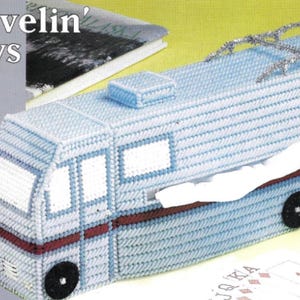 Pode incluir: Uma capa para caixa de lenços de tecido plástico azul e branco em forma de autocaravana com um porta-bagagem prateado no topo. O título "Travelin' Days" está impresso na frente da capa.