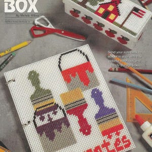 May include: A white plastic canvas with a colorful paintbrush and paint can design. The canvas is labeled "notes" and is part of a craft kit for making a pencil box.