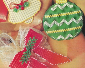May include: Three handmade Christmas ornaments made with plastic canvas. A white bell with a red bow, a green and white striped ornament, and a red bow with a green snowflake.