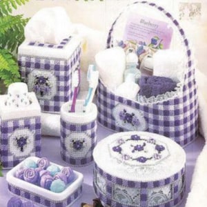 May include: A set of bathroom accessories in a purple and white gingham pattern. The set includes a tissue box cover, a toothbrush holder, a soap dish, a round box, and a basket with the word "Blueberry" on it.