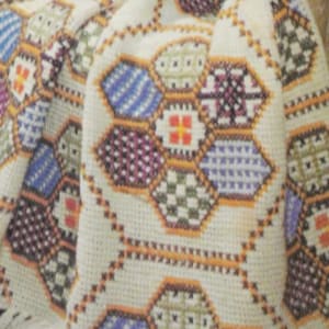 May include: A white crocheted blanket with a colorful geometric pattern. The pattern features hexagons with different colored squares inside. The colors include purple, blue, green, orange, and white.